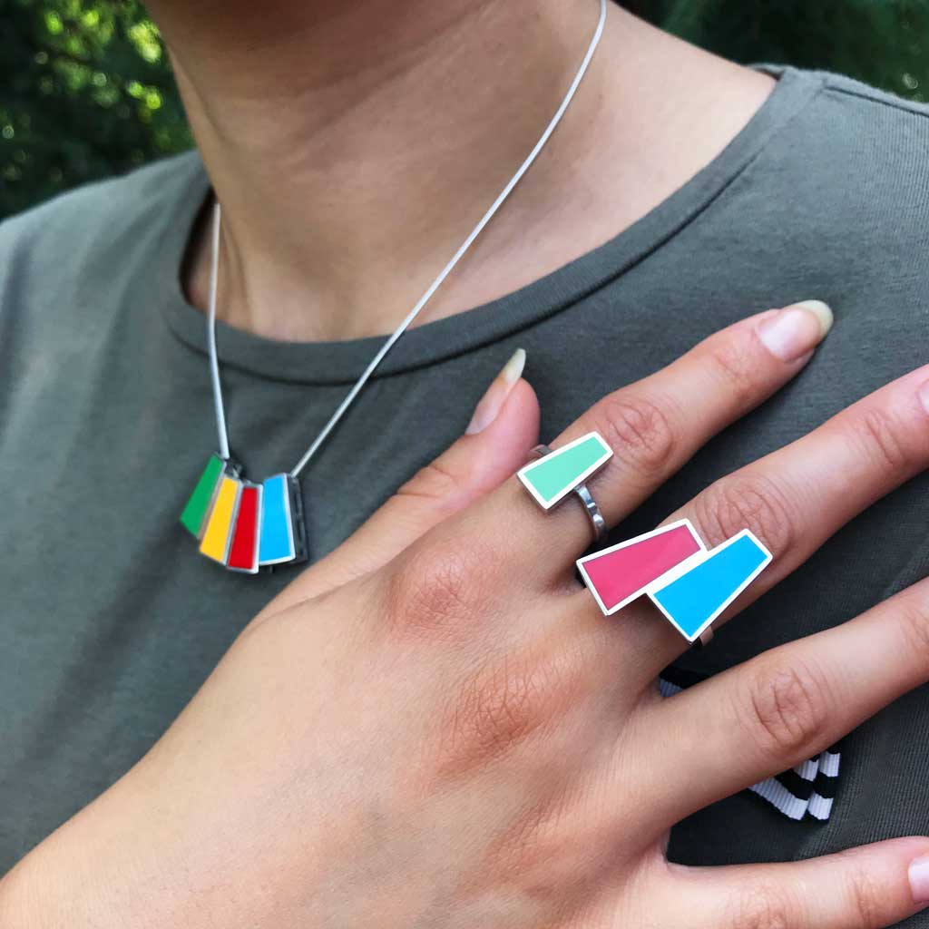 A models wearing handcrafted silver necklace and rings embellished with vibrant yellow, blue, red, and green vitreous enamel, showcasing modern craftsmanship with traditional design elements.