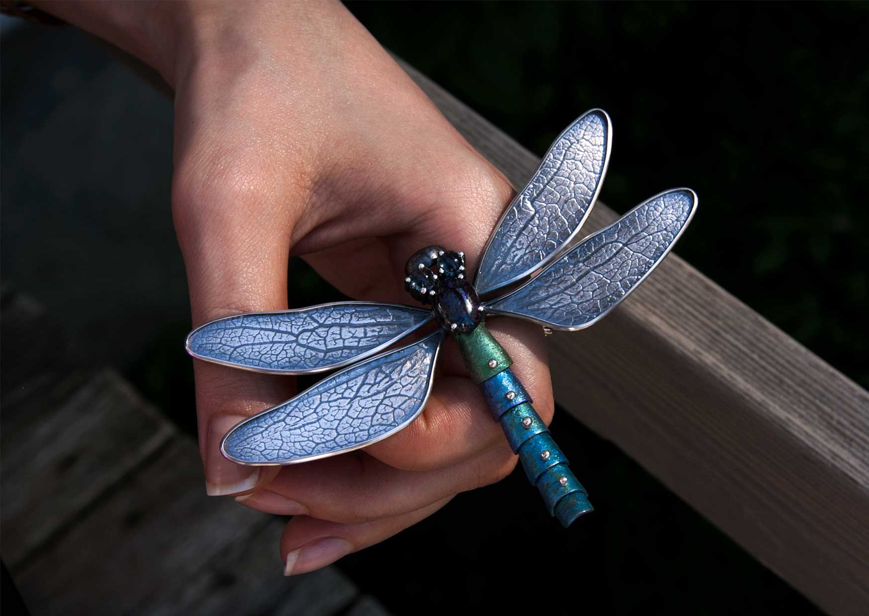 Hand holding a colorful dragonfly silver brooch, showcasing bespoke craftsmanship and intricate enamel detailing by Mahroz Hekmati.