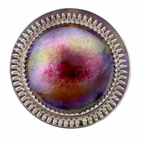 Handmade sterling silver circular brooch with full spectrum vitreous enamel in purples, blues, reds, oranges and golds on white background